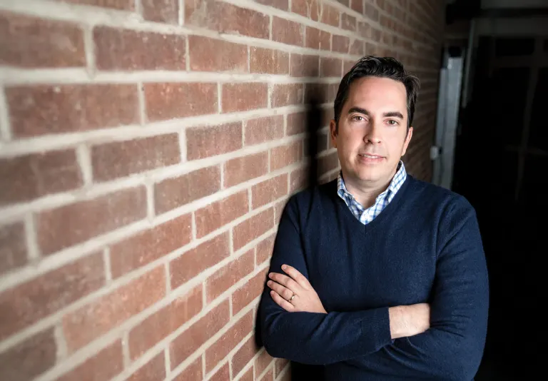 John Machacek, Chief Innovation Officer for the Greater Fargo Moorhead Economic Development Corporation, leaning against a brick wall with his arms crossed.