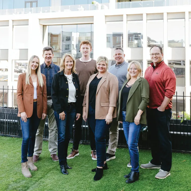 Alyssa Lakosky with her JBC Commercial Real Estate teammates standing together on a rooftop lawn in front of a downtown building.