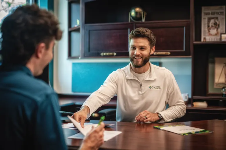 A Capital Credit Union employee reviews paperwork with a member across a desk.