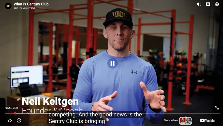 Man in a black cap and blue pullover speaking to camera in a gym, with a video caption naming Neil Keltgen, founder and coach