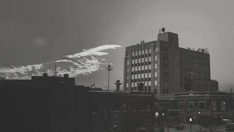 Cityscape with a tall brick building, smaller structures, and a street scene under a cloudy sky.
