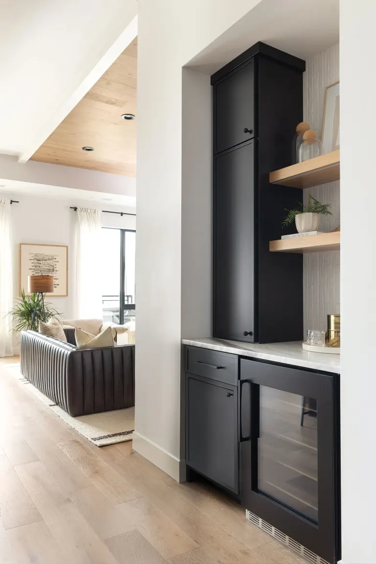 Tall black built-in cabinet with marble countertop, open shelves, and a glass-front wine cooler in a bright living space.