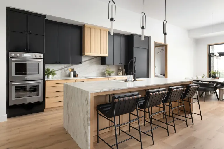 Modern kitchen with black cabinets, wooden island, and stainless steel appliances; row of bar stools along the island.