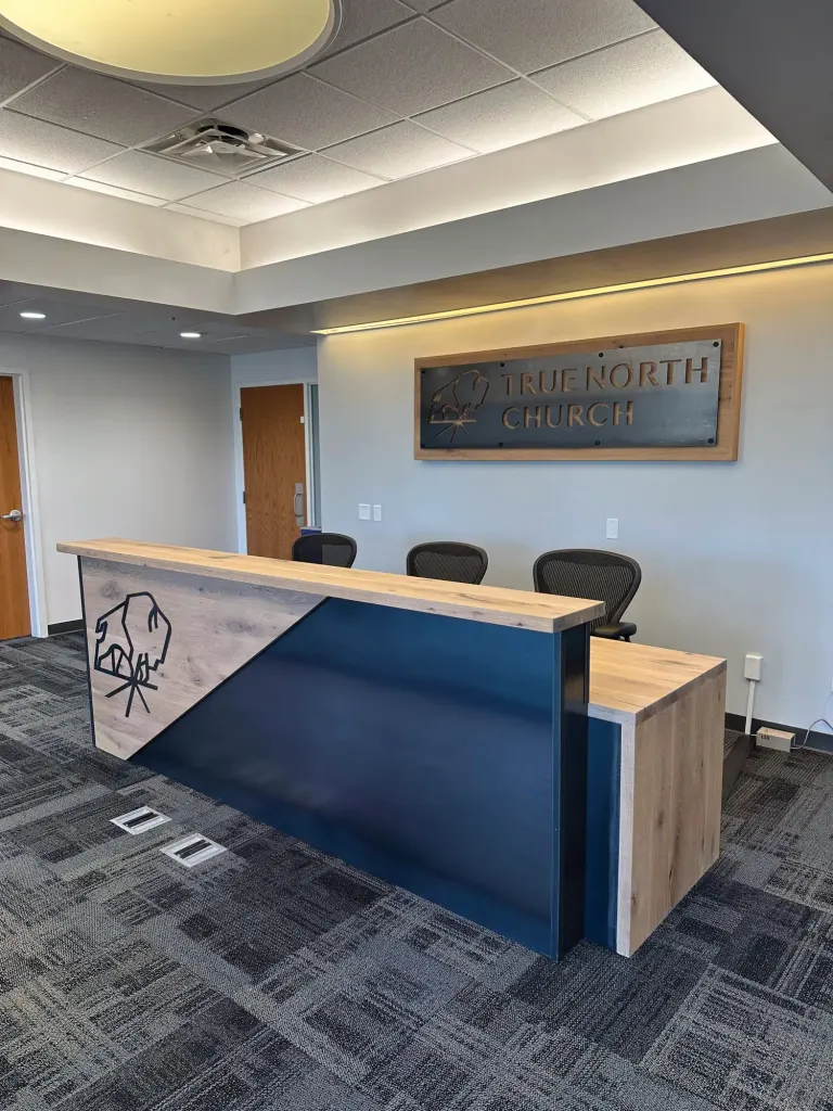 Reception desk with a wood top and a navy and wood front in front of a True North Church sign
