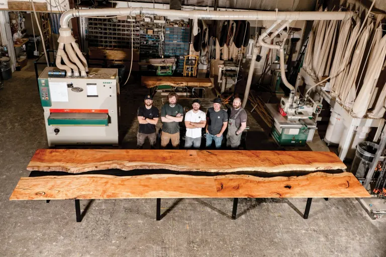 Five Grain Designs team members standing behind a live-edge table in the shop