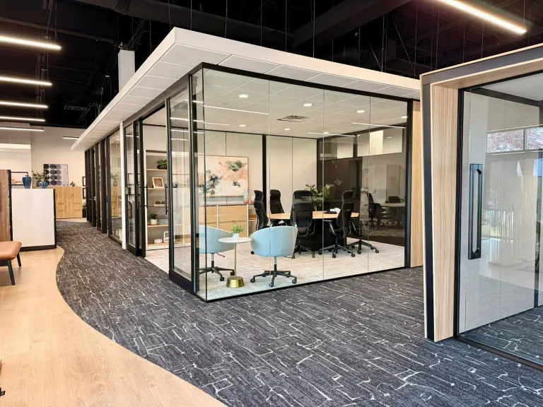 Glass-enclosed meeting room with blue and white chairs, framed in black metal with a wood accent wall