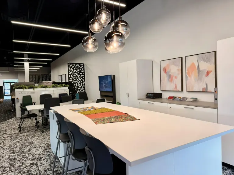 Long white work table with stools and pendant lights, art on the wall and a screen in the background