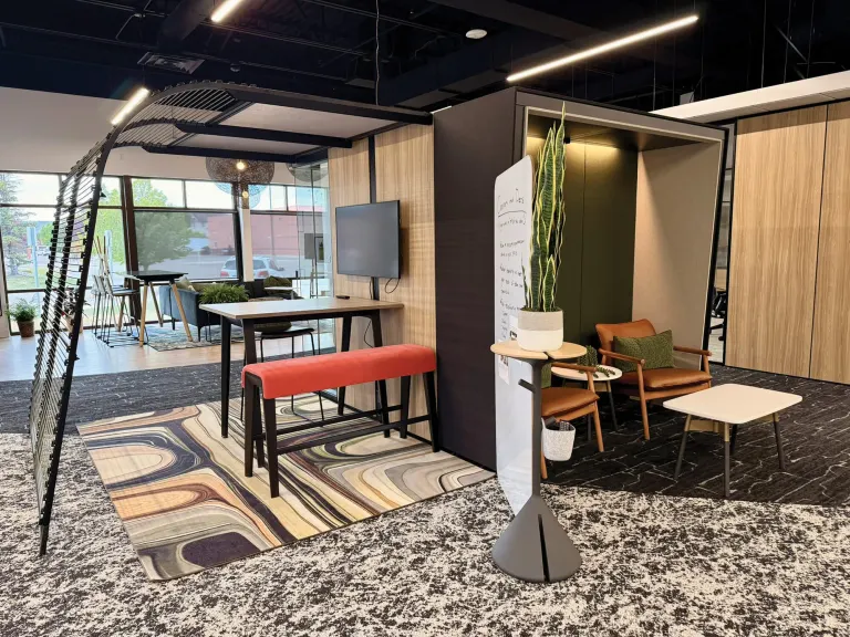 Collaboration area with a high-top table, red bench, rust armchair, patterned rug and a rolling whiteboard