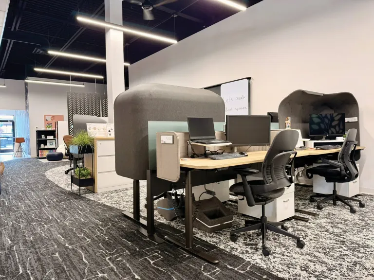 Workstation with a sit-stand desk, privacy panels, monitors and ergonomic task chairs on patterned carpet
