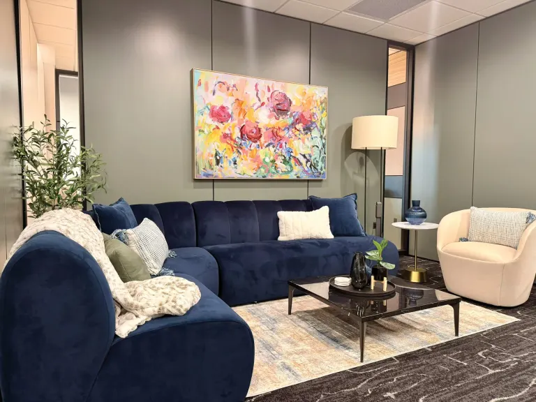 Lounge with a navy sectional sofa, cream swivel chair, floor lamp and a colorful floral painting on a gray wall
