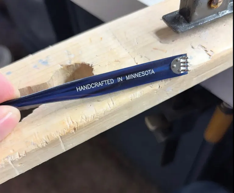 Pencil labeled Handcrafted in Minnesota rests on rough wooden workbench with metal tool nearby.