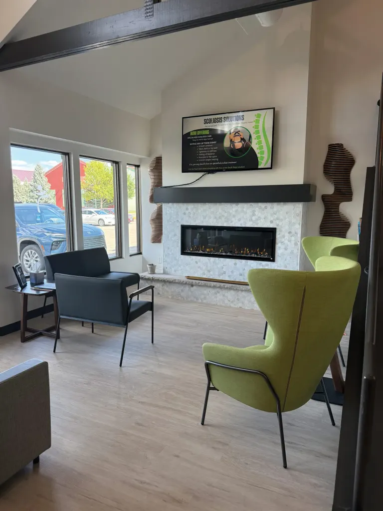 Bright waiting area with a green wingback chair, black armchair and a linear fireplace under a wall-mounted screen