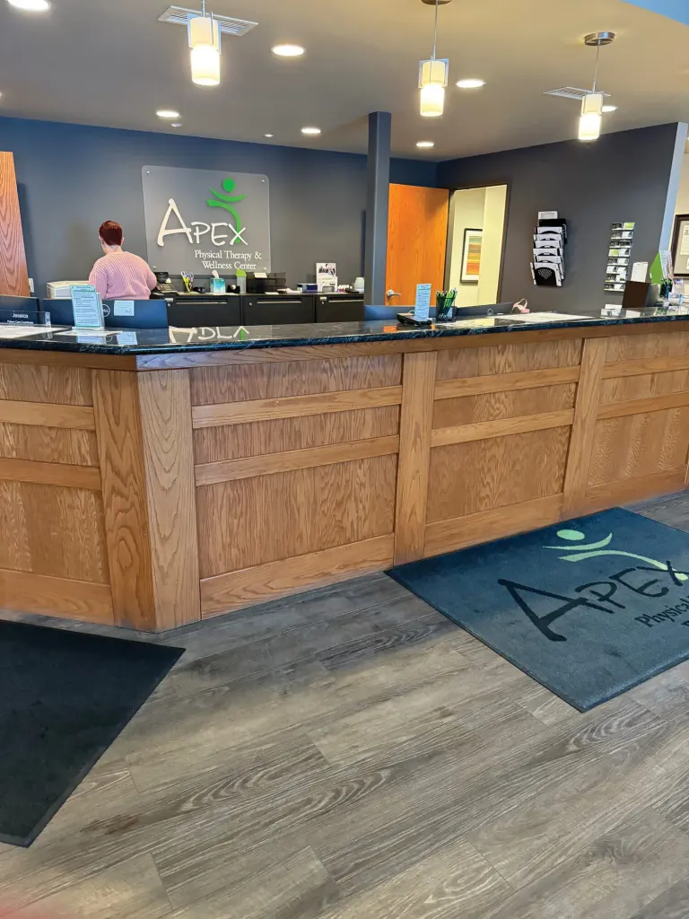 Wood front desk with a granite top and an Apex floor mat on gray wood-look flooring