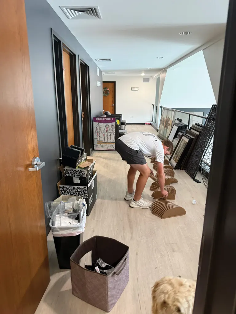 Person bending down to sort items in a hallway with framed art leaning against the wall