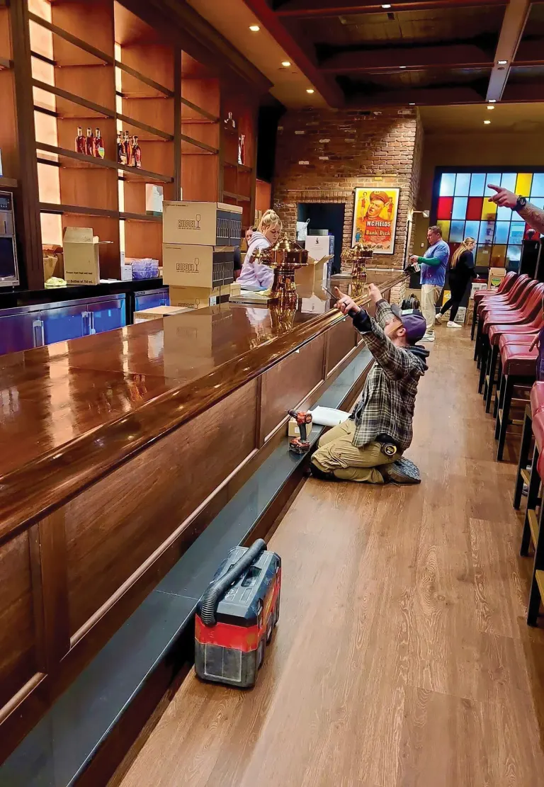 Worker kneeling beside a long polished wood bar in a nearly finished restaurant space
