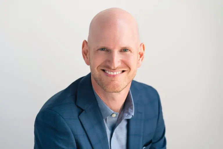 Portrait of Mike Meagher, smiling, wearing a blue plaid blazer
