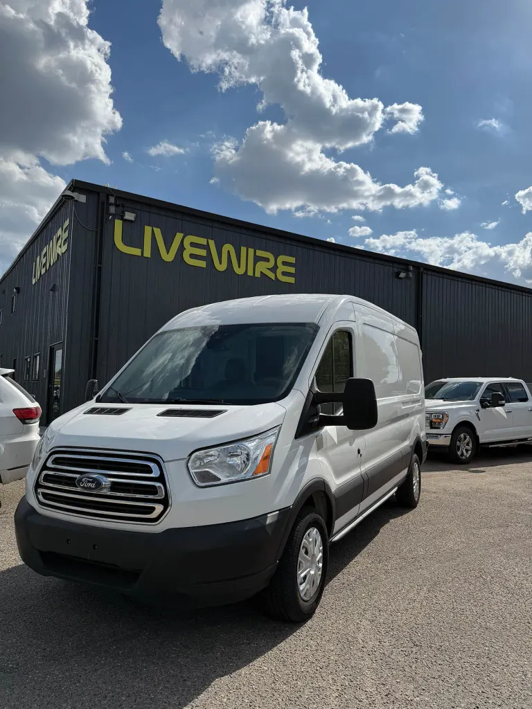 White Ford Transit van parked outside a dark building with large yellow “LIVEWIRE” sign under a blue sky.