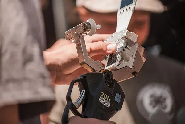 Person holding a handheld tool with metal clamp and blade, assembling a metallic component.