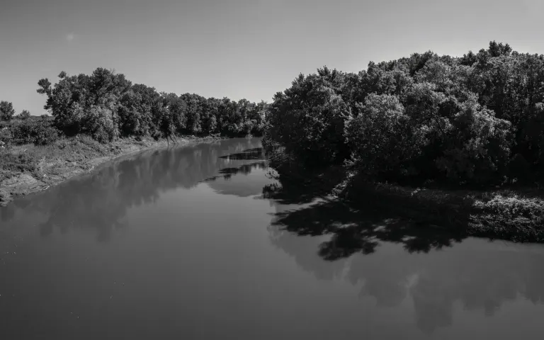 Black and white view of a river winding between tree-lined banks under a clear sky