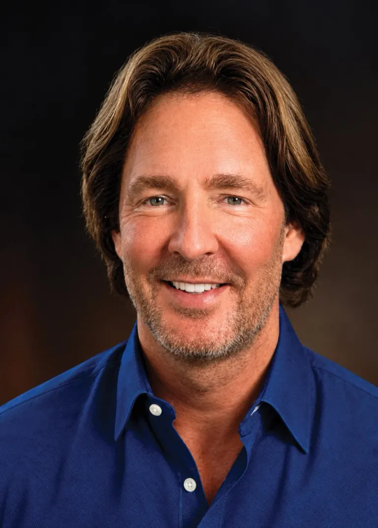 Ace Brandt smiling in a blue collared shirt in a head-and-shoulders portrait.