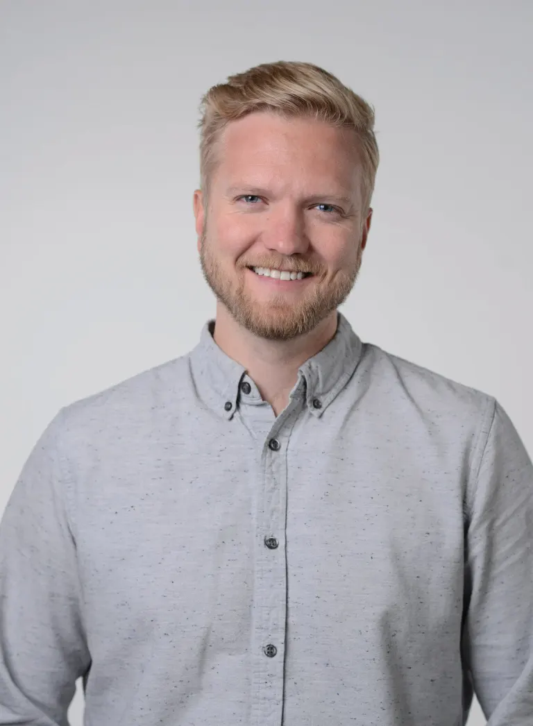 Austin Morris smiling in a light gray button-up shirt against a gray background.