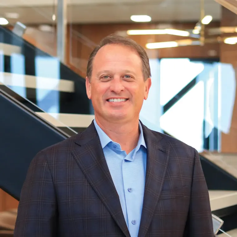 Jeff Laliberte smiling in a dark blazer and light blue shirt in front of a modern office staircase.
