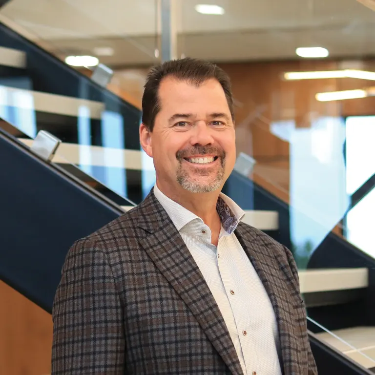 Jim Bullis smiling in a plaid blazer in front of a modern office staircase.