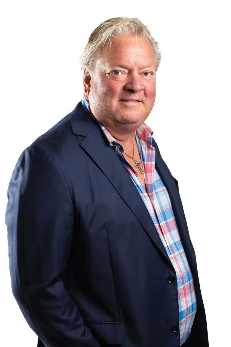Tyler Brandt in a navy blazer and plaid shirt with one hand in his pocket, against a white background.