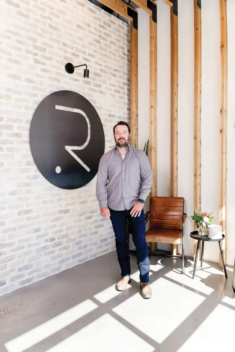 David Reid standing beside the Radiant Homes logo on a white brick wall