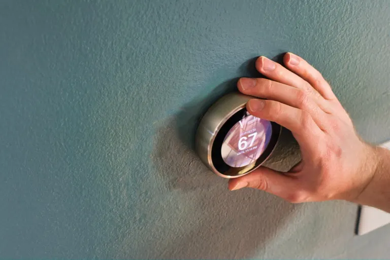 Hand turning a smart thermostat on a teal wall